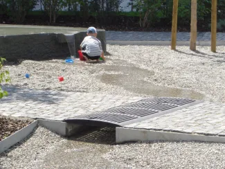Der Quellstein ist Mittelpunkt des Kinderspielplatzes im ersten Innenhof und gleichzeitig Funktionselement zur Regenwasserbewirtschaftung. Spielendes Kind an Quelle