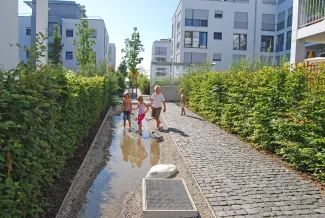 Der Wasserlauf, der sich hier gemütlich durch die Innenhöfe schlängelt, nimmt bei Regen sämtliches Niederschlagswasser in das System auf. Kinder spielen am Wasserlauf